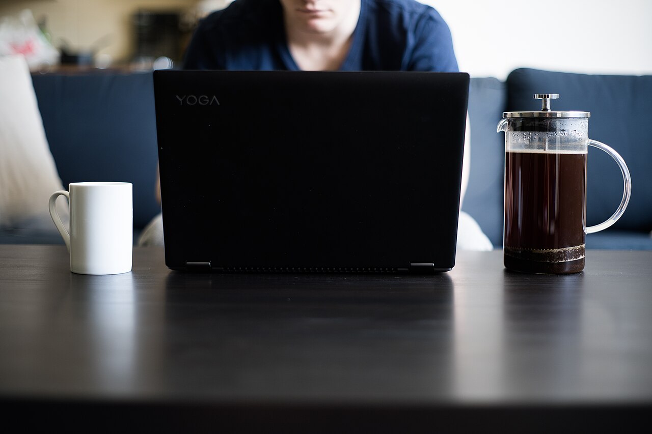 Person working on a laptop at a table with a mug and a French press