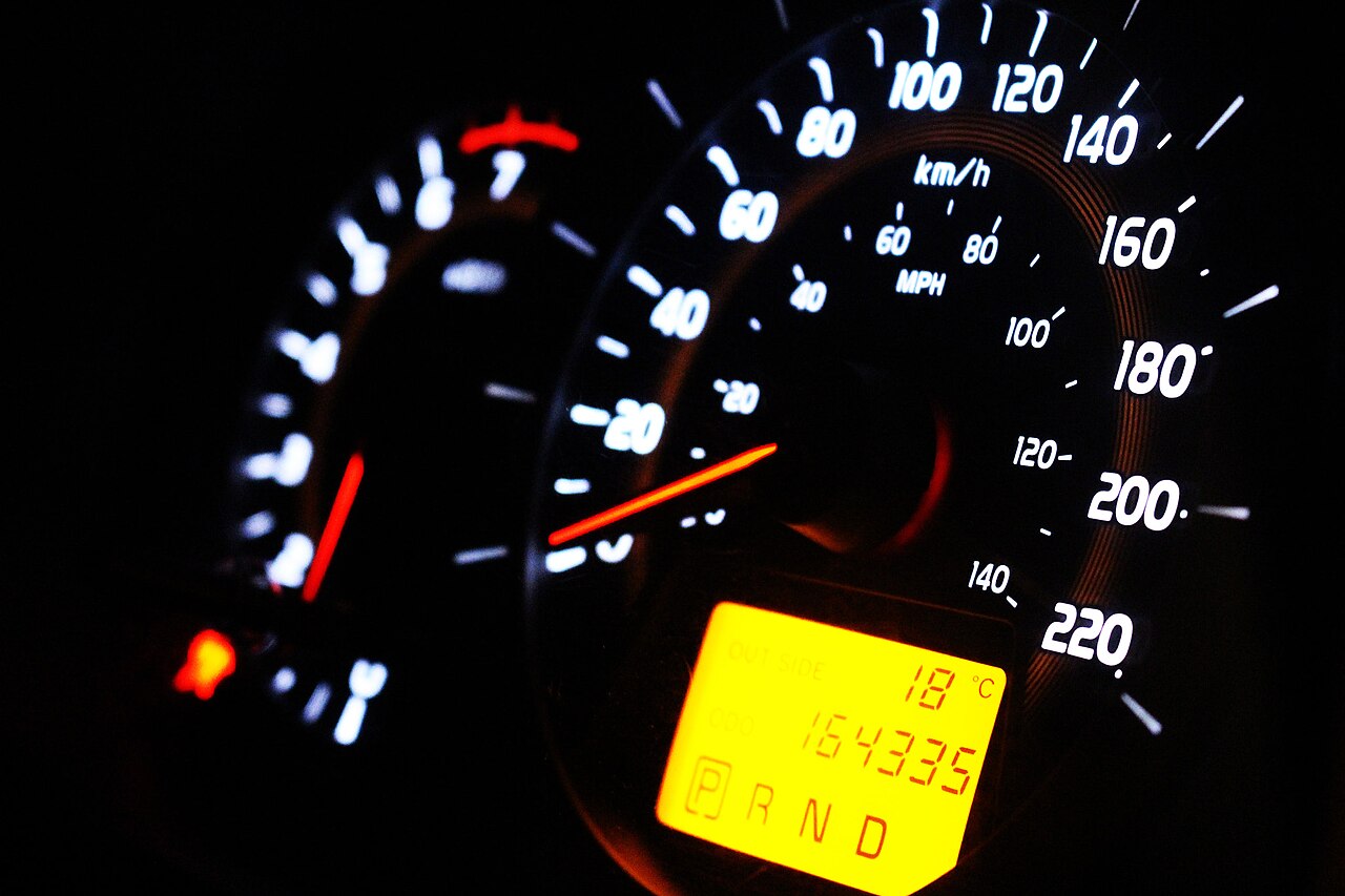 Illuminated car speedometer dial glowing against a dark dashboard