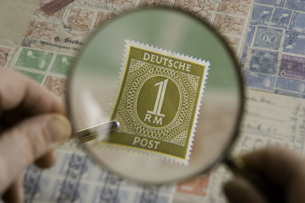 Magnifying glass enlarging a postage stamp in a collection