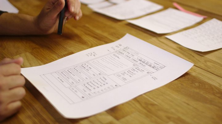 Hand-drawn paper prototype of a website user interface on a table