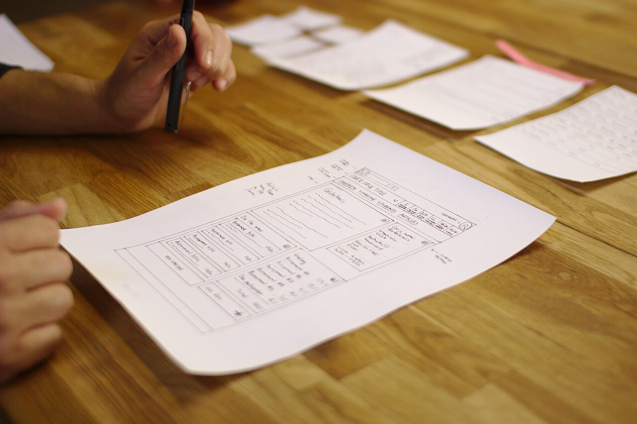 Hand-drawn paper prototype of a website user interface on a table