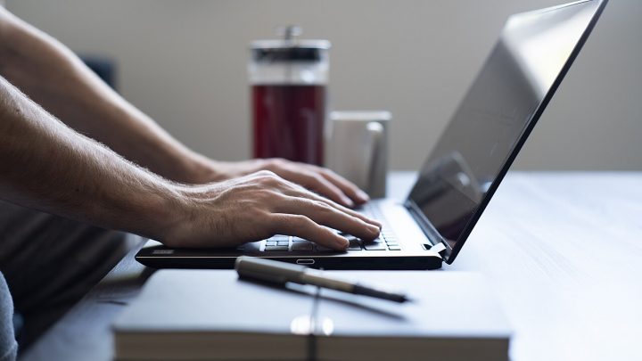 Person typing on a laptop at a desk with notepad and drink
